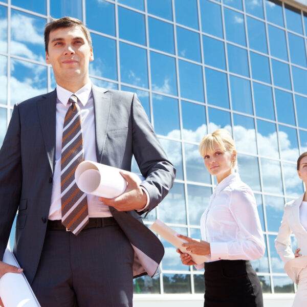 Portrait,Of,Successful,Leader,Holding,Rolled,Papers,With,Two,Employees